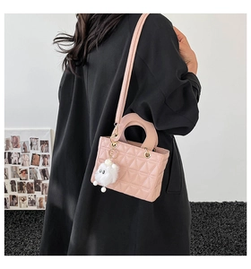 Gros plan du sac bandoulière rose matelassé avec pendentif monstre peluche et poignée ronde