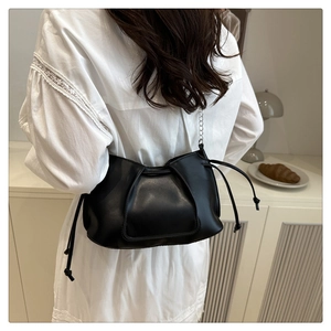 Detail of black pleated shoulder bag with drawstrings and silver chain on model