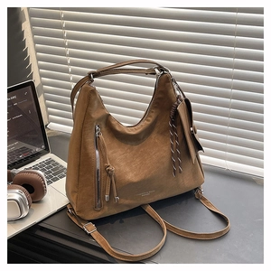 Détail d'un sac en daim marron avec gland tissé et zip latéral dans un décor de bureau sobre