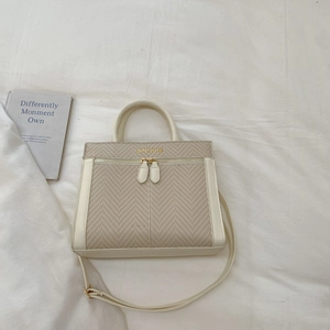 Détail du sac beige avec texture en chevrons et logo doré sur le devant du sac à main