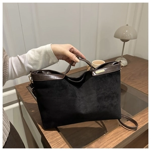Close-up of black suede tote bag with brown leather handles and gold-tone metal hardware