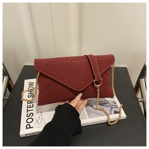 Détail du sac enveloppe rouge foncé avec texture tricotée et bandoulière en chaîne dorée
