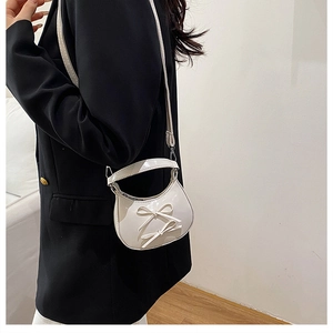 Détail du mini sac demi-lune blanc brillant avec nœuds et garnitures argentées