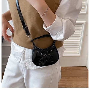 Mini black crescent handbag featuring a bow detail worn by a model in a minimal setting