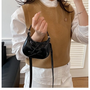 Sac chic en cuir verni noir à nœuds, porté avec un gilet beige et une chemise blanche