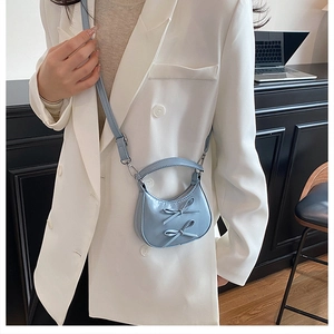 Détail du sac croissant bleu clair avec nœuds porté par un mannequin en costume blanc