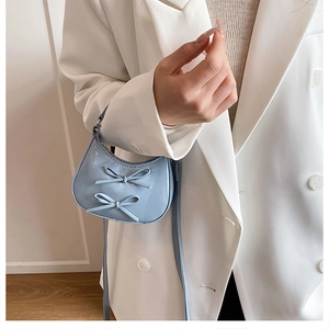 Détail du sac demi-lune en cuir verni bleu clair avec nœuds 3D porté avec un costume blanc