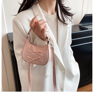 Détail d'un mini sac rose brillant avec nœuds décoratifs tenu par un mannequin en blazer