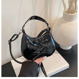 Détail du sac croissant noir verni avec deux nœuds et une fine bandoulière