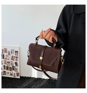 Detail of dark brown leather crossbody bag with suede flap and gold metal handle