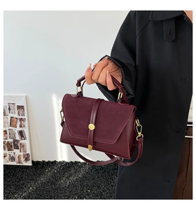 Detail of burgundy leather crossbody bag featuring suede stitching and a gold round buckle