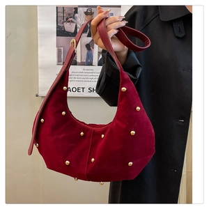 Macro view of burgundy velvet crescent bag featuring decorative gold metal rivets