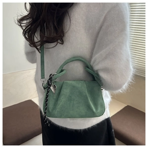 Détail du sac à main en daim vert avec plis, breloque cœur et ruban rayé sur la bandoulière