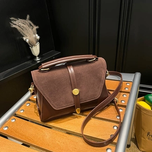 Brown vintage leather crossbody bag with suede patchwork on a rustic wooden bench