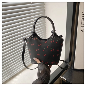 Detail van de zwarte lederen tas met kersenprint, geknoopte handgreep en lange schouderband