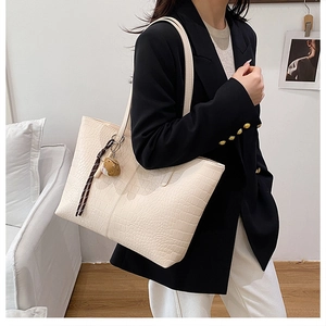 Detail of cream tote bag with crocodile embossing, shoulder strap and bear charm