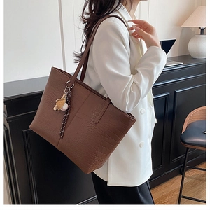Detail of dark brown tote bag featuring crocodile texture and stylish bag charm