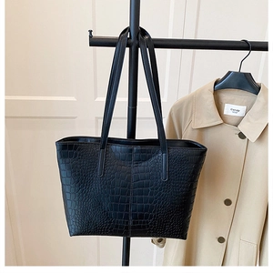 Detail of black crocodile pattern tote bag featuring premium leather texture and long straps
