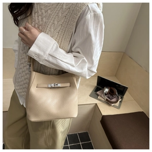 Detail of beige lychee leather bucket bag with silver twist lock on female model