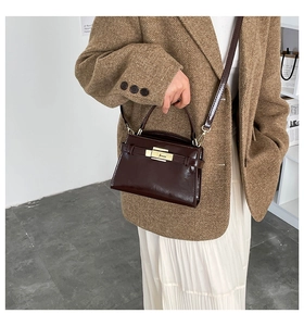 Close-up of dark brown patent leather box bag with gold lock on a female model