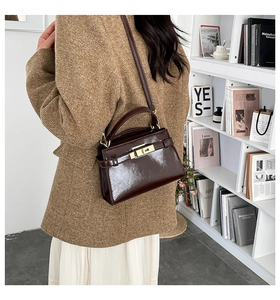 Detail of dark brown polished leather shoulder bag with gold metal clasp on a model