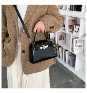 Detail of glossy black leather handbag with golden twist lock and adjustable shoulder strap