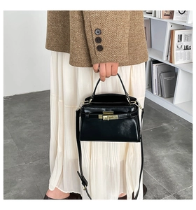 Close-up of black glossy leather handbag with metal turn-lock and slim shoulder strap