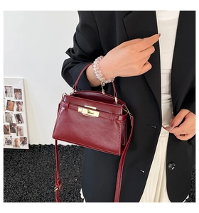 Detail of burgundy glossy leather handbag with golden metal turn-lock and shoulder strap