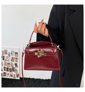Detail of burgundy glossy leather handbag with gold twist lock and top handle