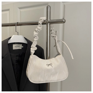 Detail of white crescent bag featuring ruched handle and silver butterfly charm