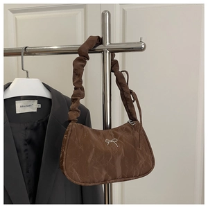 Detail of a brown moon bag featuring a silver metal bow and pleated scrunchie strap