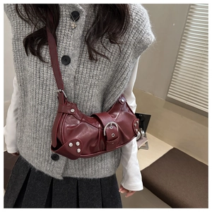 Dark red crescent crossbody bag with silver buckle and rivets shown on a model