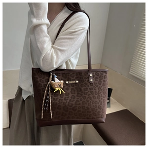 Close-up of leopard print tote bag with gold logo plaque and cute bear charm detail