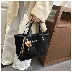 Detail of leopard print tote bag featuring a metal Fashion plaque and brown bear charm