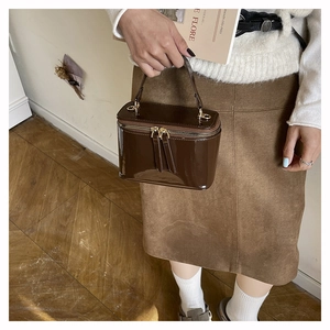 Detail of dark brown patent leather box bag with dual metal zippers and single handle