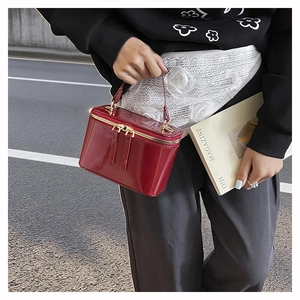 Detail of burgundy patent leather square box bag with gold zipper held by model