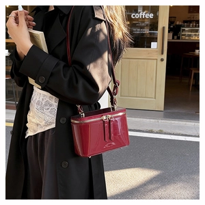 Detail shot of a burgundy patent leather box bag with dual zippers and smooth mirror finish