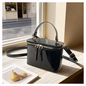 Detail of glossy black patent leather box bag with gold-tone hardware and top handle