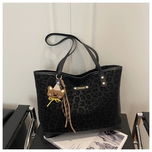 Macro detail of black leopard print tote bag with gold metal logo and bear charm