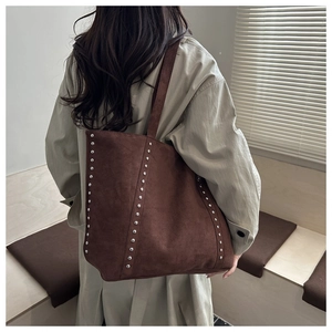 Detail of dark brown suede tote bag with silver rivets carried over shoulder