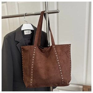 Detail of silver rivets on dark brown suede tote bag hanging in a fashion display