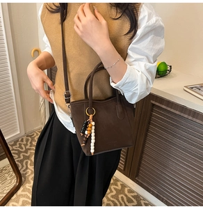 Detail of a dark brown matte leather bucket bag with colorful wooden beaded charm