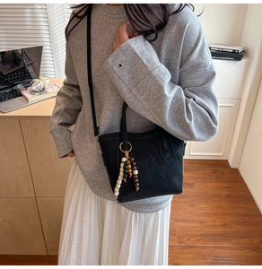 Détail du sac seau noir avec pompon en perles de bois et poignée en cuir sur un bureau