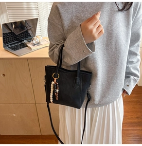 Détail d'un sac seau noir mat avec un gland de perles colorées et une bandoulière