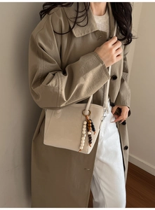 Close-up of beige crossbody bucket bag with decorative wooden beads and tassel detail