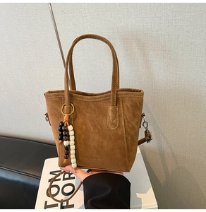 Detail of a brown suede tote bag with decorative colorful beads and top handles