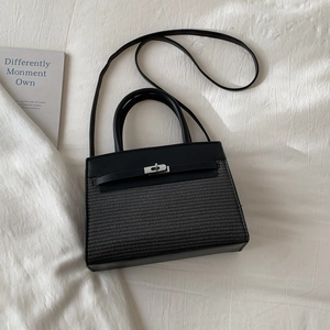 Top-down view of a black leather patchwork handbag with silver lock on white bedding