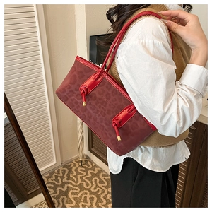 Close-up of burgundy tote bag featuring leopard texture and gold metallic knot detail