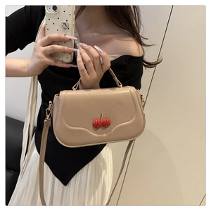 Detail of beige crossbody bag with red rhinestone cherry motif and long strap
