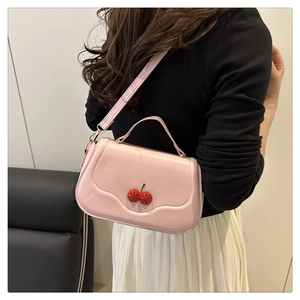 Close-up of pink crossbody bag featuring a decorative red cherry metal buckle detail